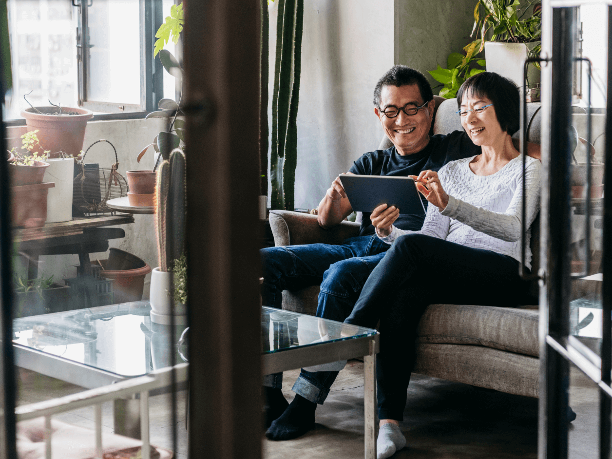 Mature man and woman sitting on sofa, view through open glass door, smiling and happy