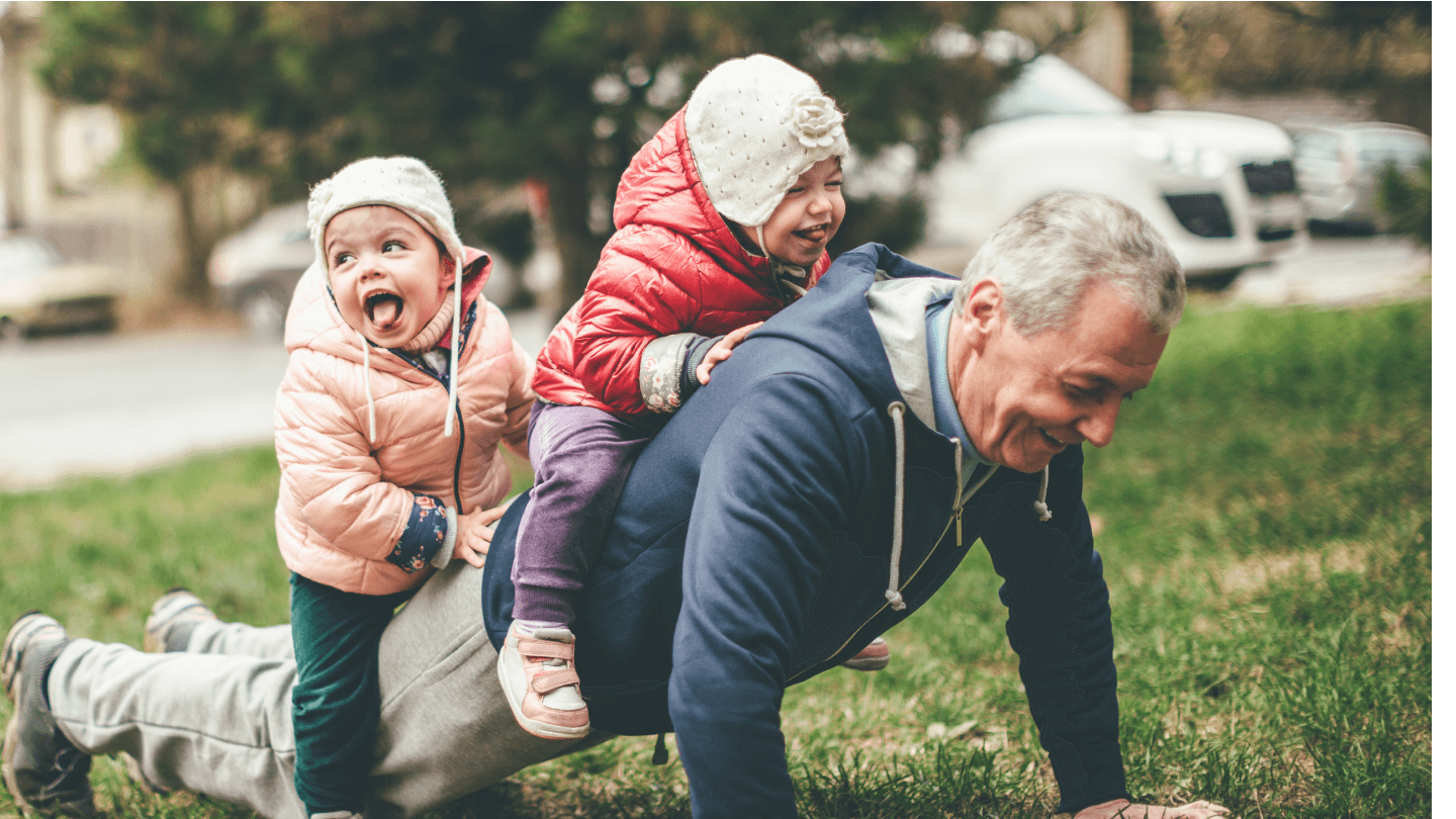 A photo of a playful grandfather and granddaughter. They are casually dressed and playing in the park. They exercise together. A grandfather is exercising while granddaughters are sitting on his back.