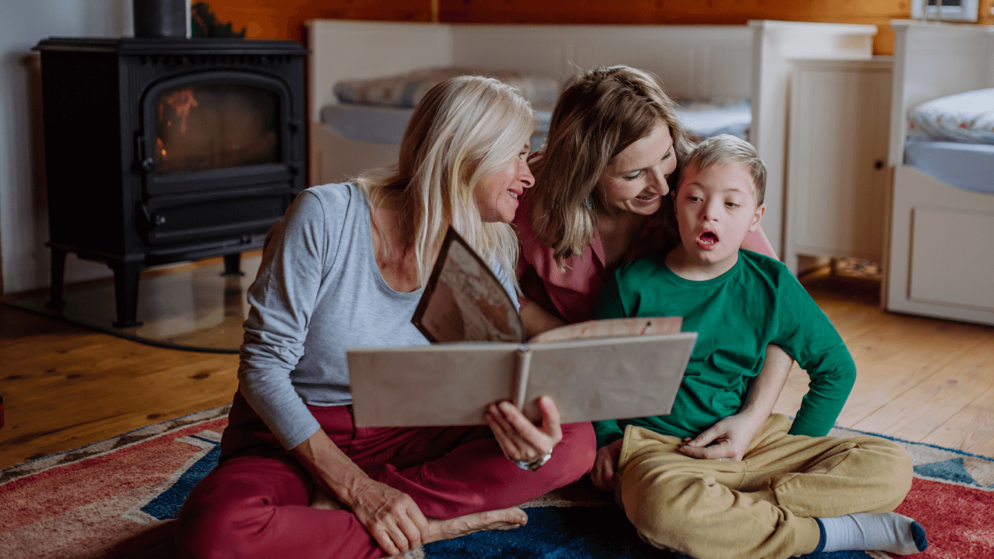 A boy with Down syndrome with his mother and grandmother looking at family photo album at home.